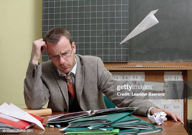 mid adult teacher at desk, paper airplane flying toward him - teacher desk foto e immagini stock