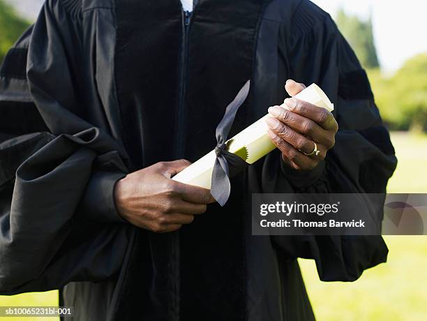 mature woman in graduation gown holding diploma, mid section - degree stock-fotos und bilder