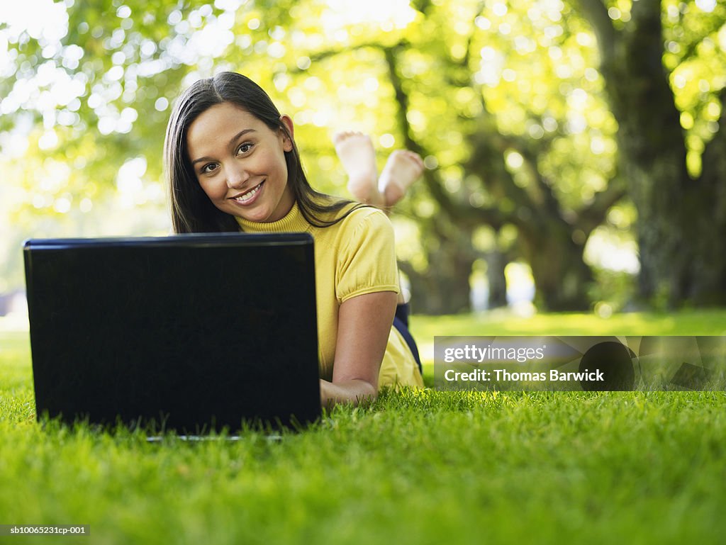 Portrait of female college student lying on grass working on laptop (surface level)