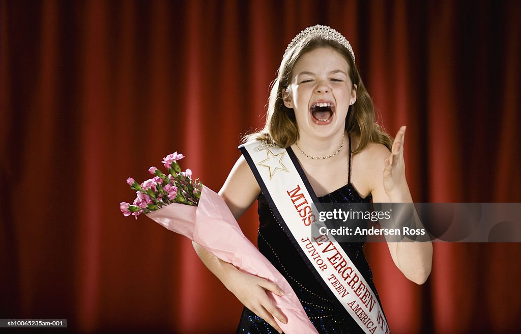 Girl (11-13) screaming on stage with bouquet of flowers in beauty pageant