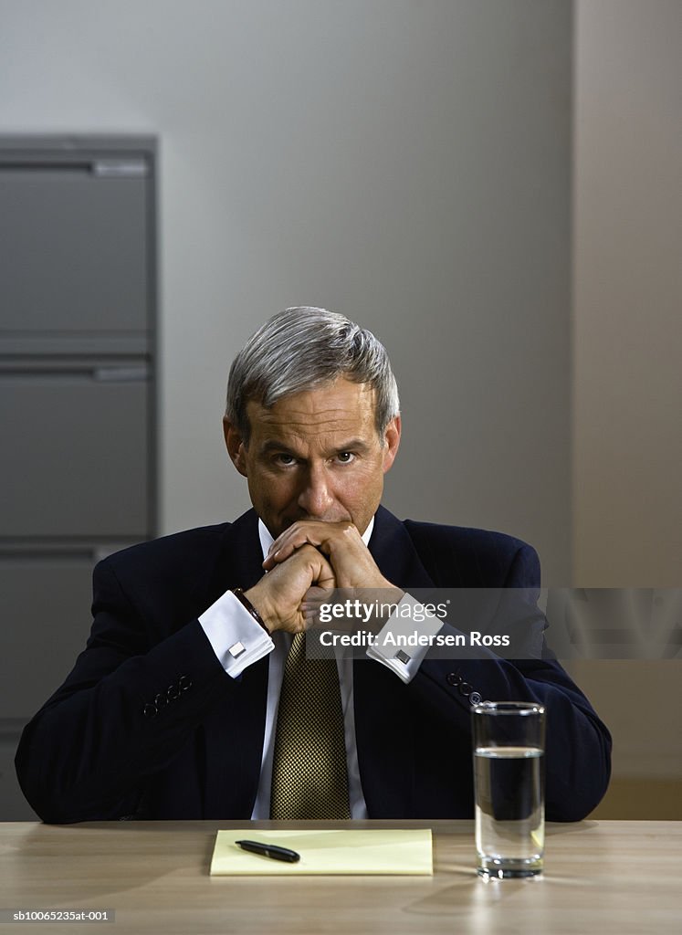 Mature businessman frowning at desk in office, portrait