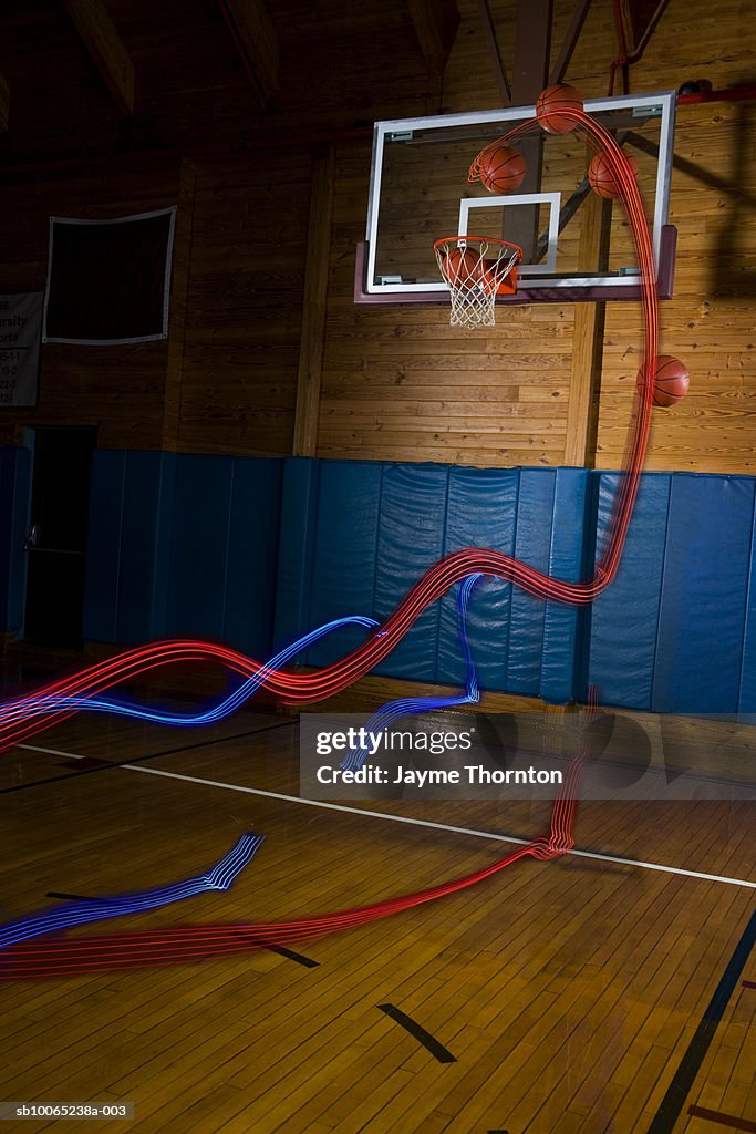 Light trails behind basketballs above indoor basketball hoop (digital composite)