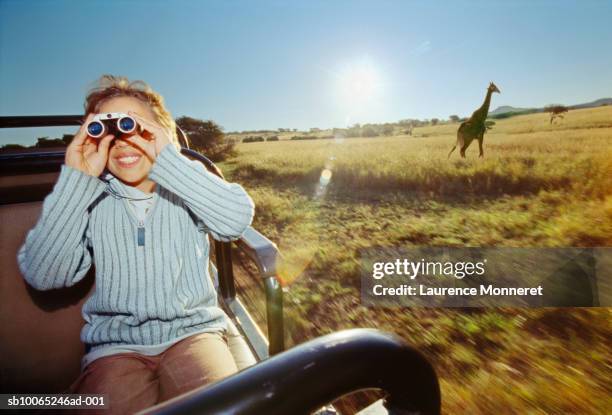 boy (8-9) in off-road vehicle, looking through binoculars, giraffe in background - kwazulu natal stock pictures, royalty-free photos & images