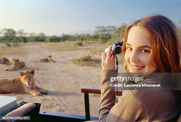 teenage girl (13-14) on safari in off-road vehicle holding binoculars, lionesses sitting in bush in background - lion africa stock-fotos und bilder