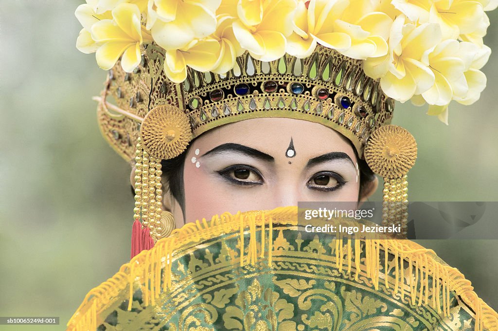 Young Balinese girl (13-14) dancer behind fan, portrait