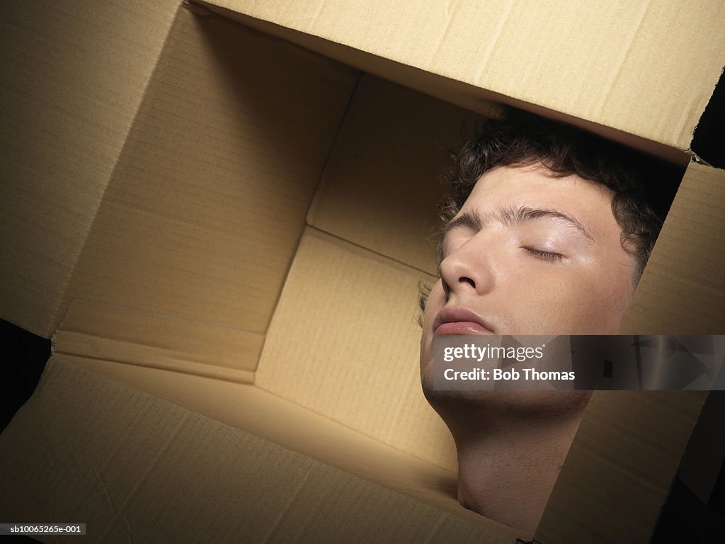 Young man head in cardboard box, eyes closed