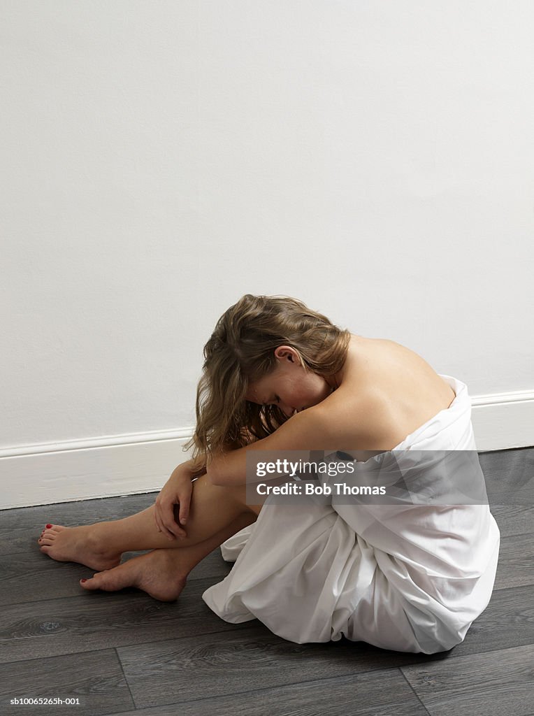 Teenage girl (16-17) wrapped in blanket resting head on knees, side view