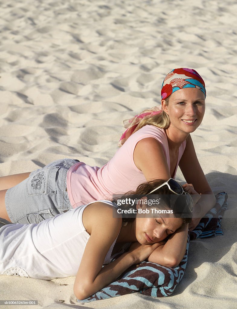 Two young women lying on sand, one sleeping