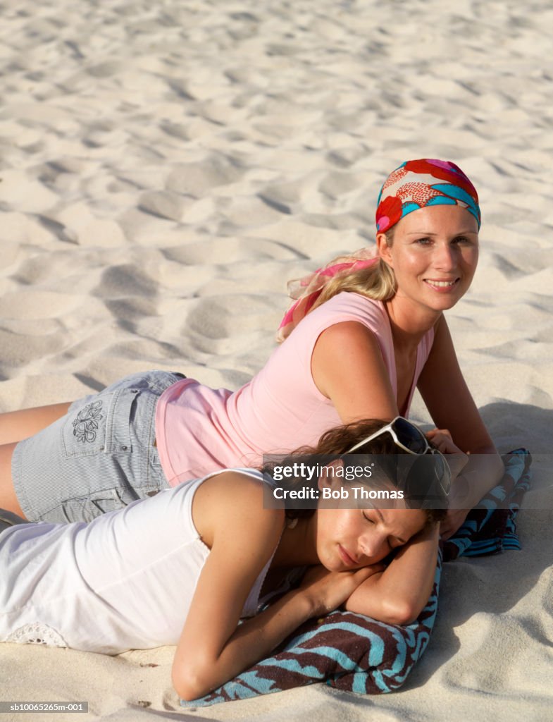 Two young women lying on sand, one sleeping