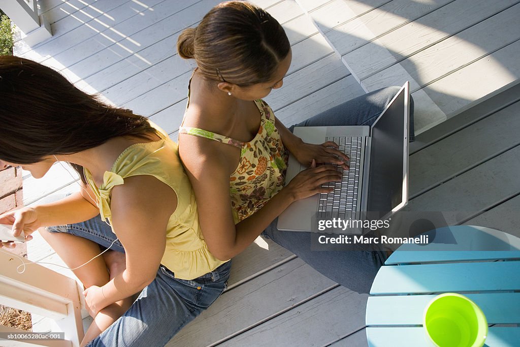 Two young women sitting on porch using wireless technology