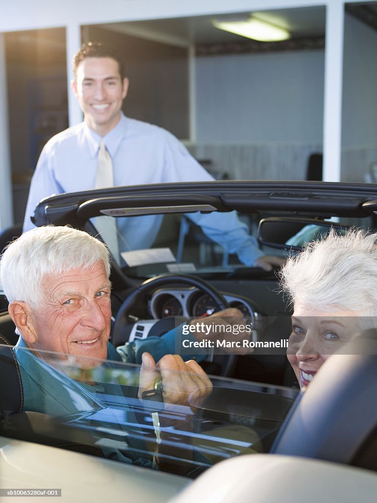 Mature woman and senior man in convertible at car dealership