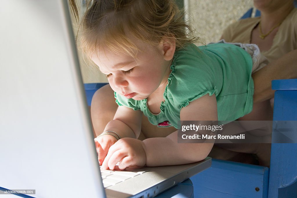 Woman holding baby girl (9-12 months) at laptop