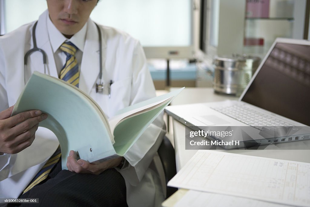 Doctor reading medical records beside laptop (cropped)