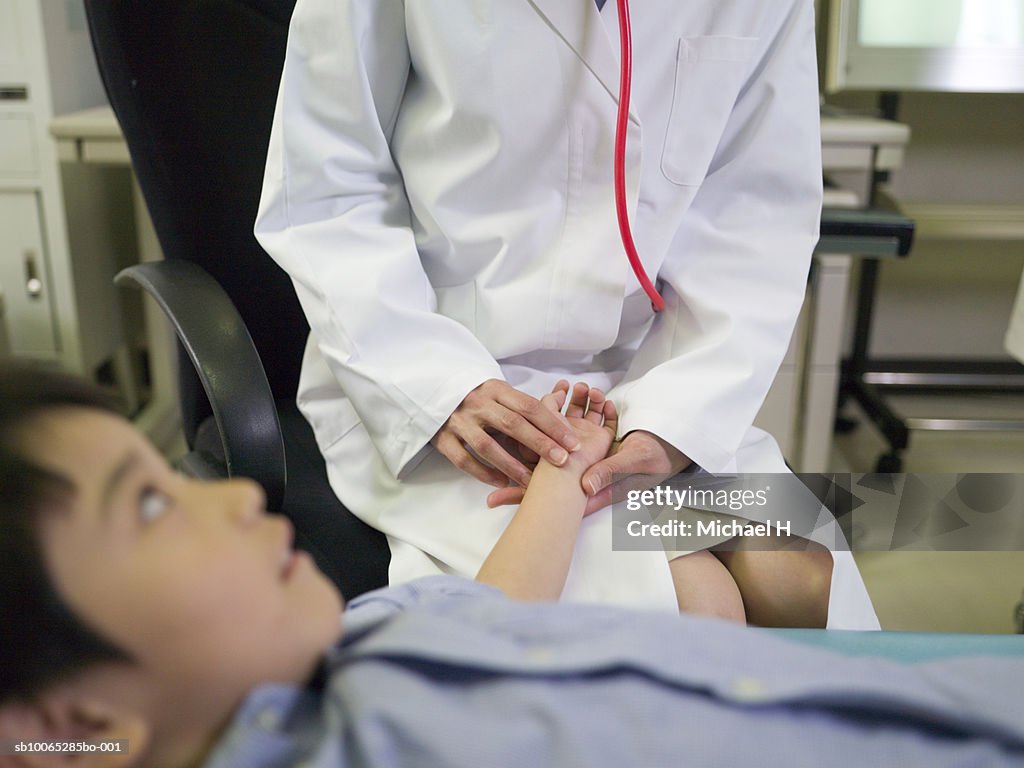 Female doctor taking child's pulse in hospital