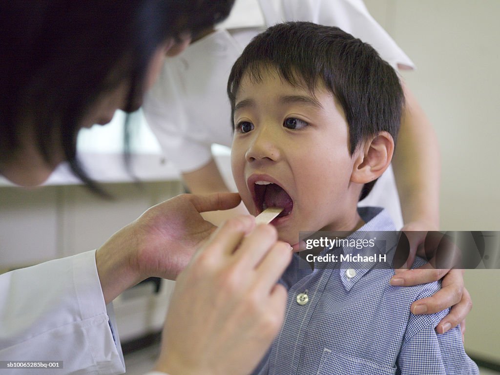 Female doctor examining mouth of boy (5-6) in hospital