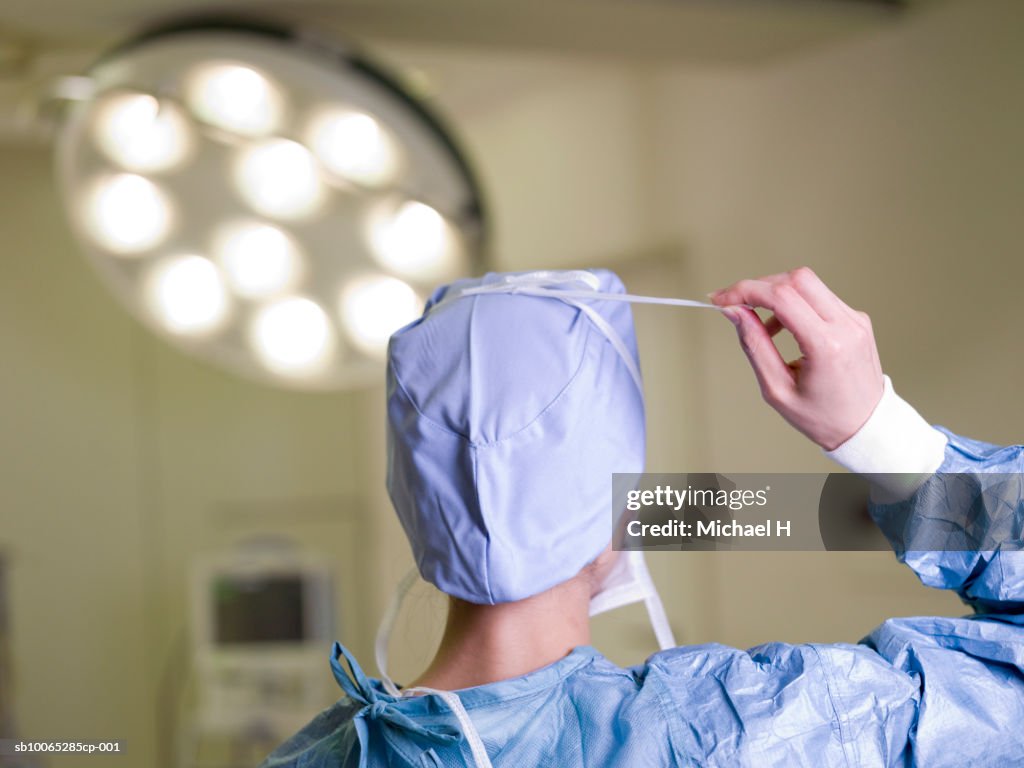 Surgeon adjusting cap in hospital, rear view