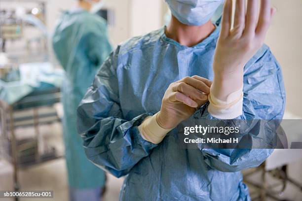 surgeon adjusting medical gloves in hospital, mid section - operationskittel stock-fotos und bilder