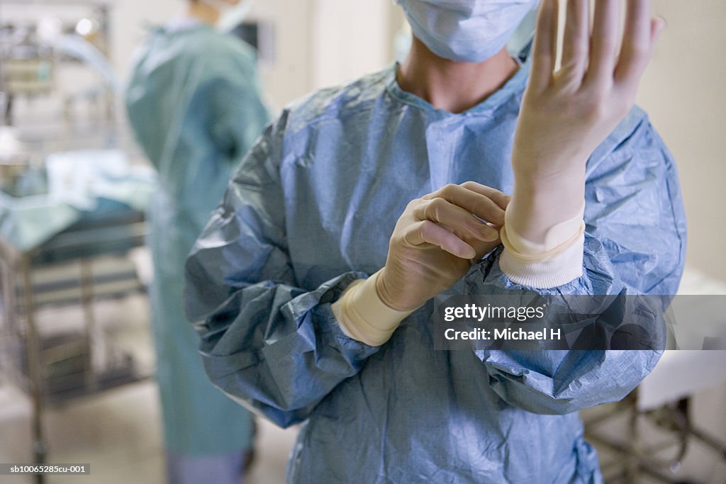 Surgeon adjusting medical gloves in hospital, mid section