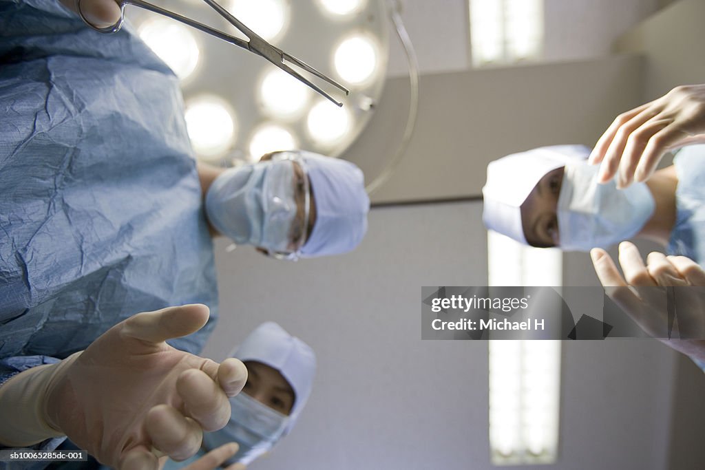 Surgeons bending over with instrument in operating room, low angle view