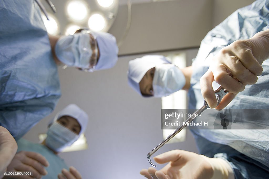 Surgeons bending over with instruments in operating room, low angle view