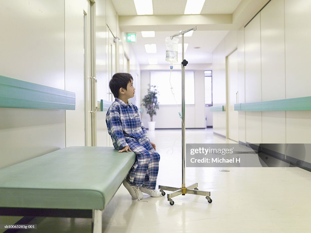 Boy (5-6) sitting with medicine drip in hospital corridor