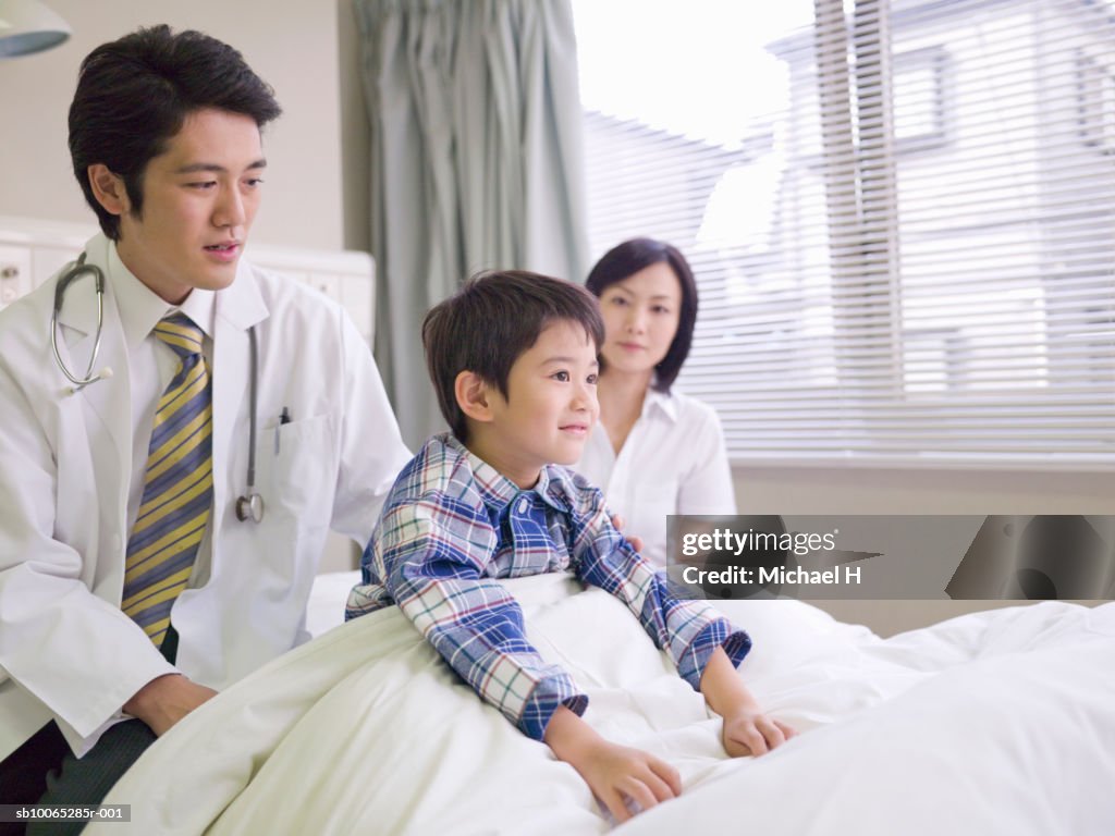 Doctor and mother with boy (5-6) in hospital bed