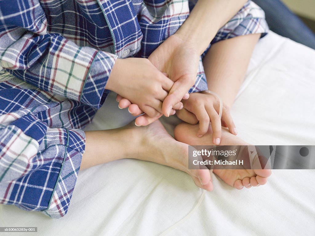 Boy (5-6) holding hands with mother on hospital bed