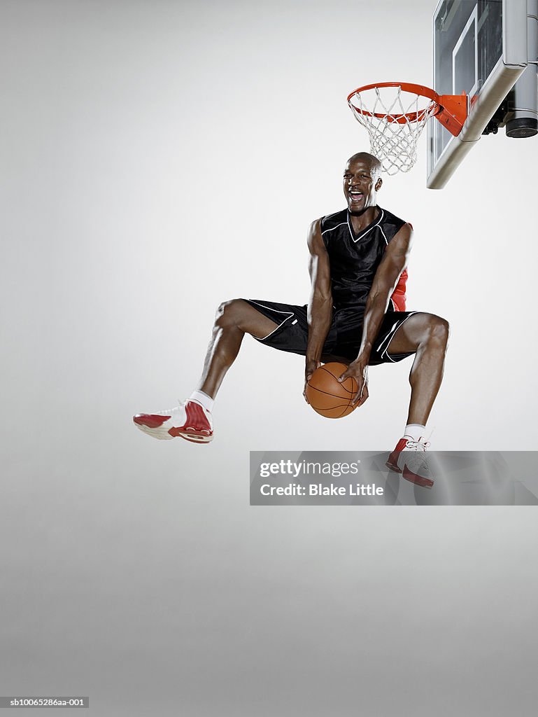 Basketball player reverse dunking basketball, low angle view