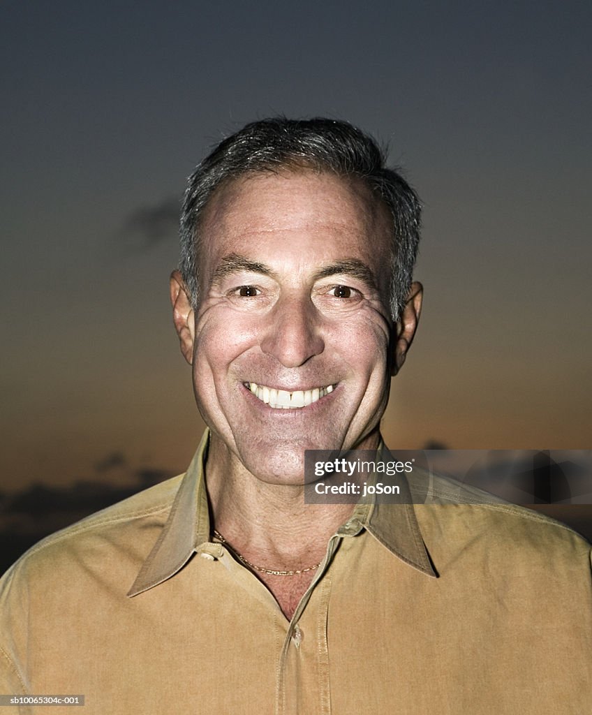 Portrait of mature man smiling, sunset sky in background