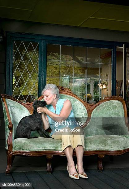 senior woman sitting on sofa at porch, kissing dog - antique sofa styles foto e immagini stock