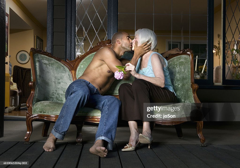 Young man and senior woman kissing on sofa at porch