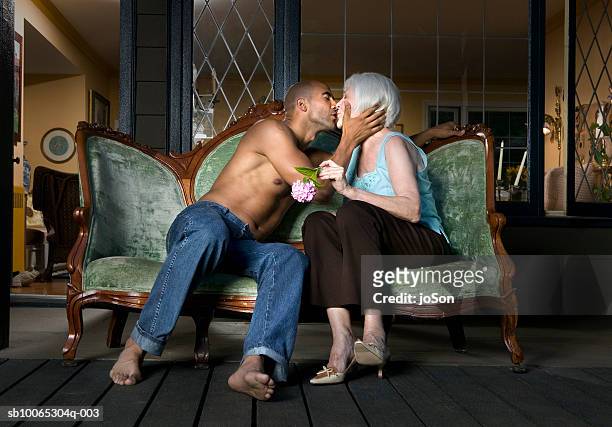 young man and senior woman kissing on sofa at porch - old woman young man fotografías e imágenes de stock