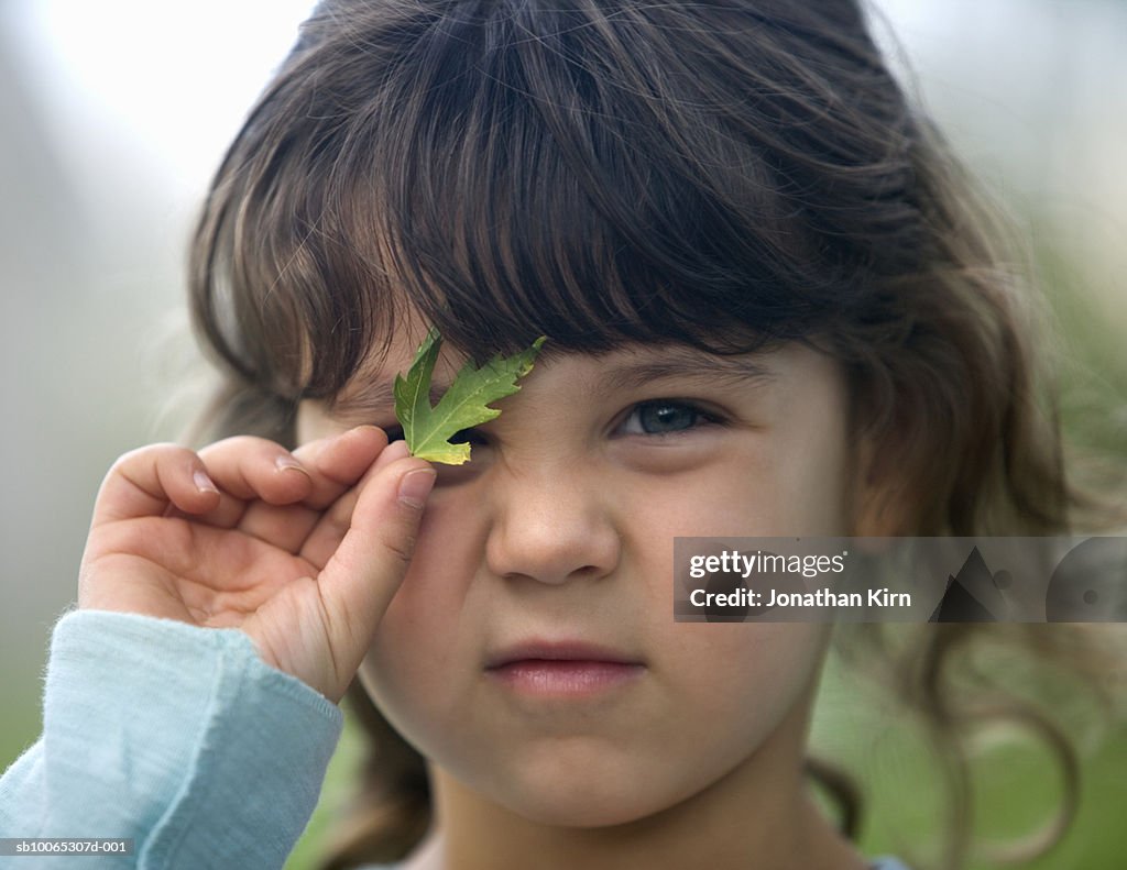 Girl (4-5) holding leaf over eye, close-up