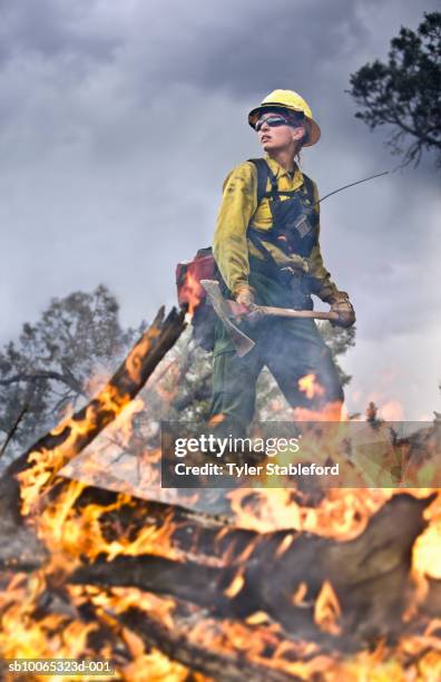 female fire-fighter holding pickaxe near burning branch - forest firefighter stock pictures, royalty-free photos & images