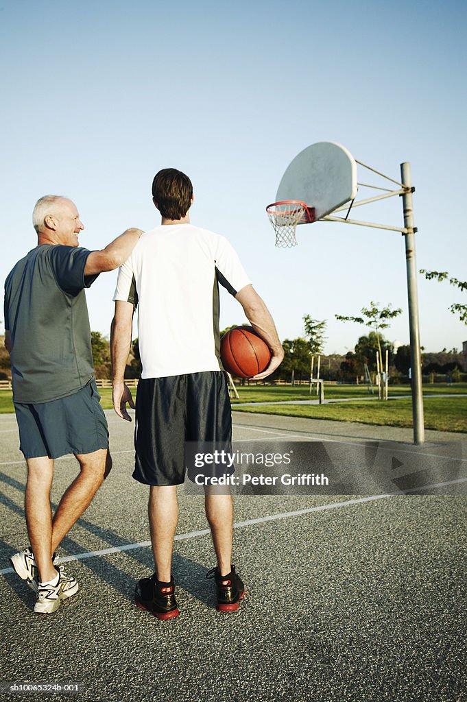 Young man and senior man on outdoor basketball court, rear view