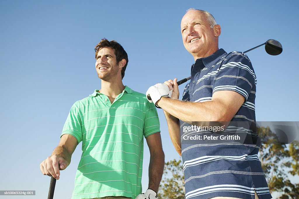 Young man and senior man holding golf clubs outdoors