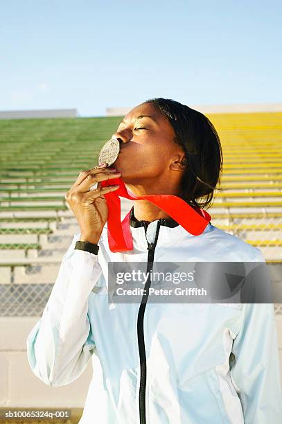 female athlete kissing medal in stadium - medalist stock pictures, royalty-free photos & images