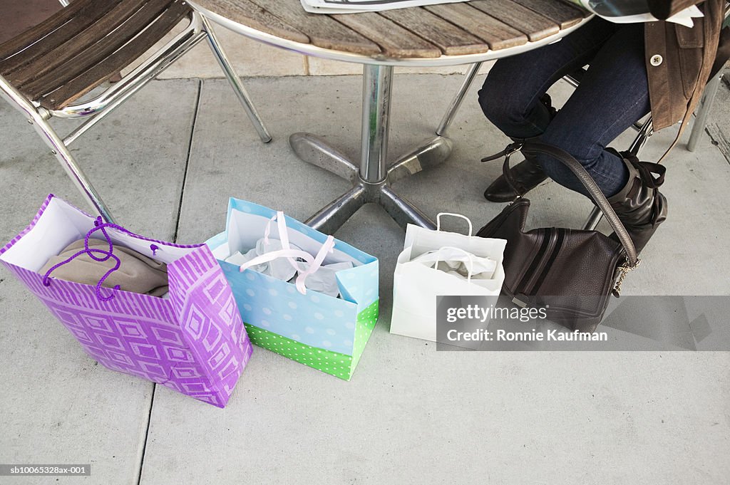 Mature woman sitting in outdoor cafT with shopping bags, low section
