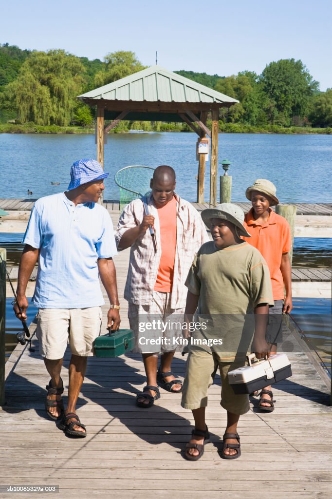 Father with three sons (11-14) walking on jetty with fishing equipment