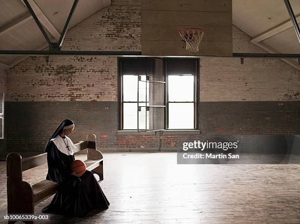 young nun sitting on bench in court holding basketball - habit clothing stock-fotos und bilder