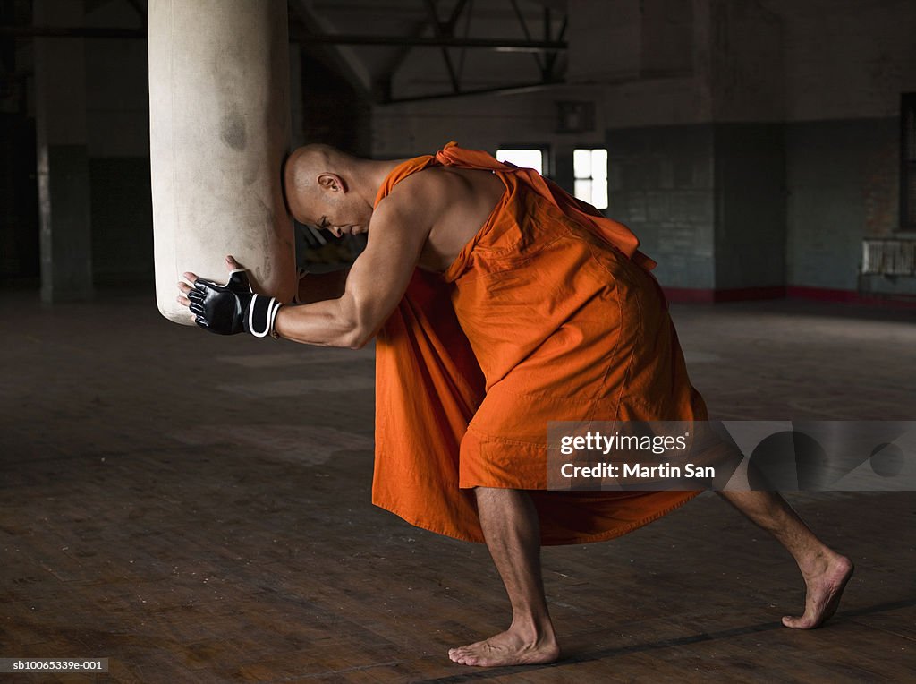 Buddhist monk leaning head on punch bag, side view