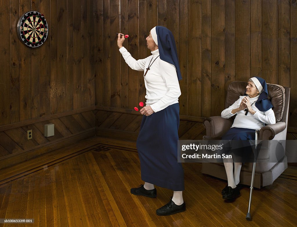 Nun playing darts and another nun watching