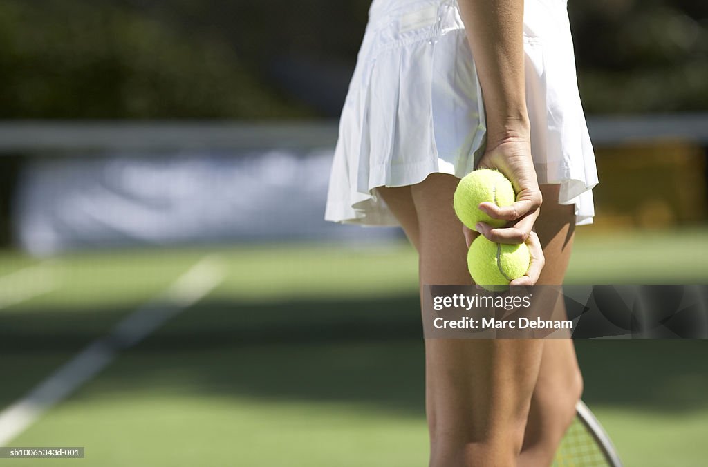 Young woman holding tennis balls on outdoor court