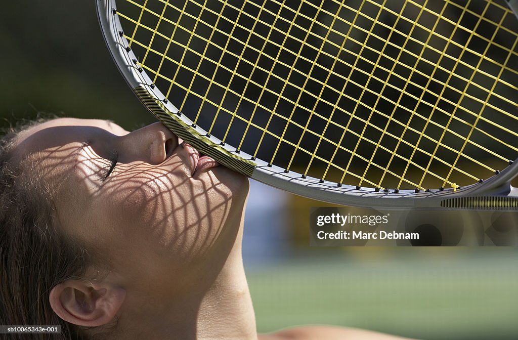 Young woman kissing tennis racket, outdoors, close-up