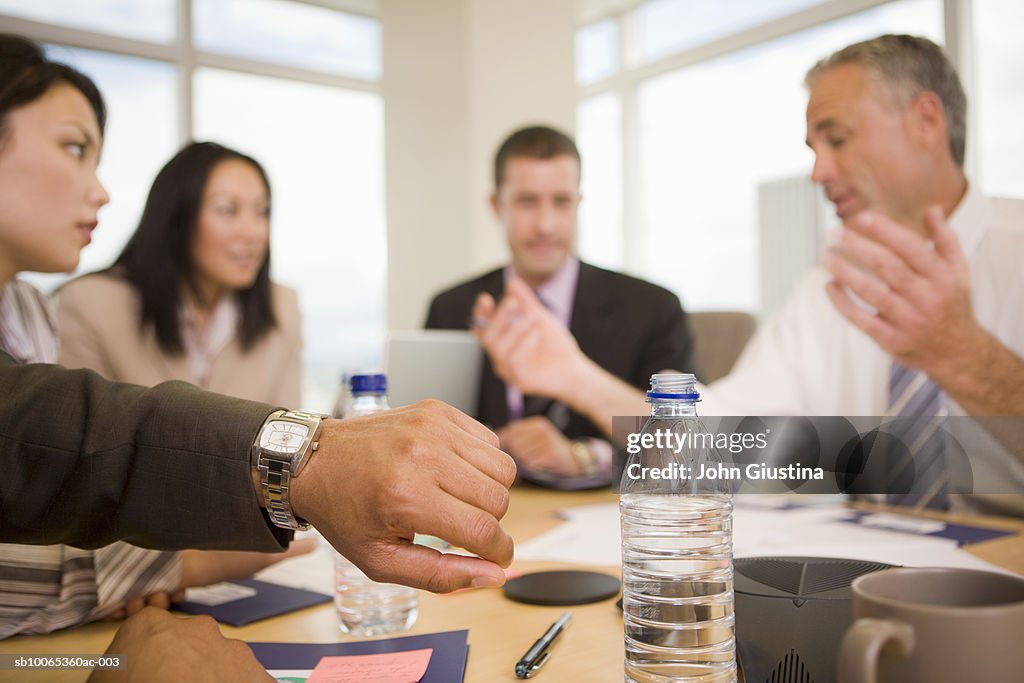 Business executives discussing at conference table, man looking at watch, (focus on foreground)