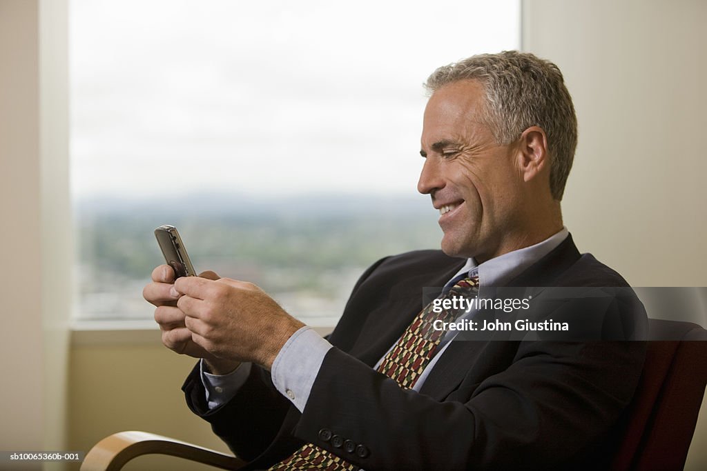 Businessman waiting in office lobby reading message, smiling