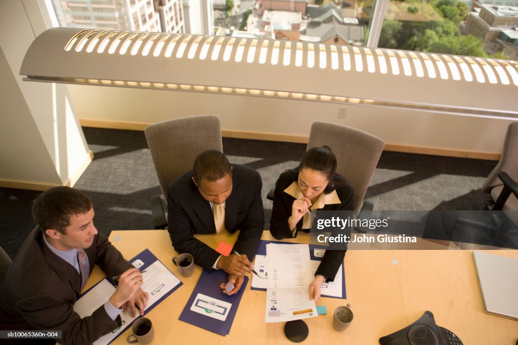 Three businesspeople looking at documents in conference room, elevated view