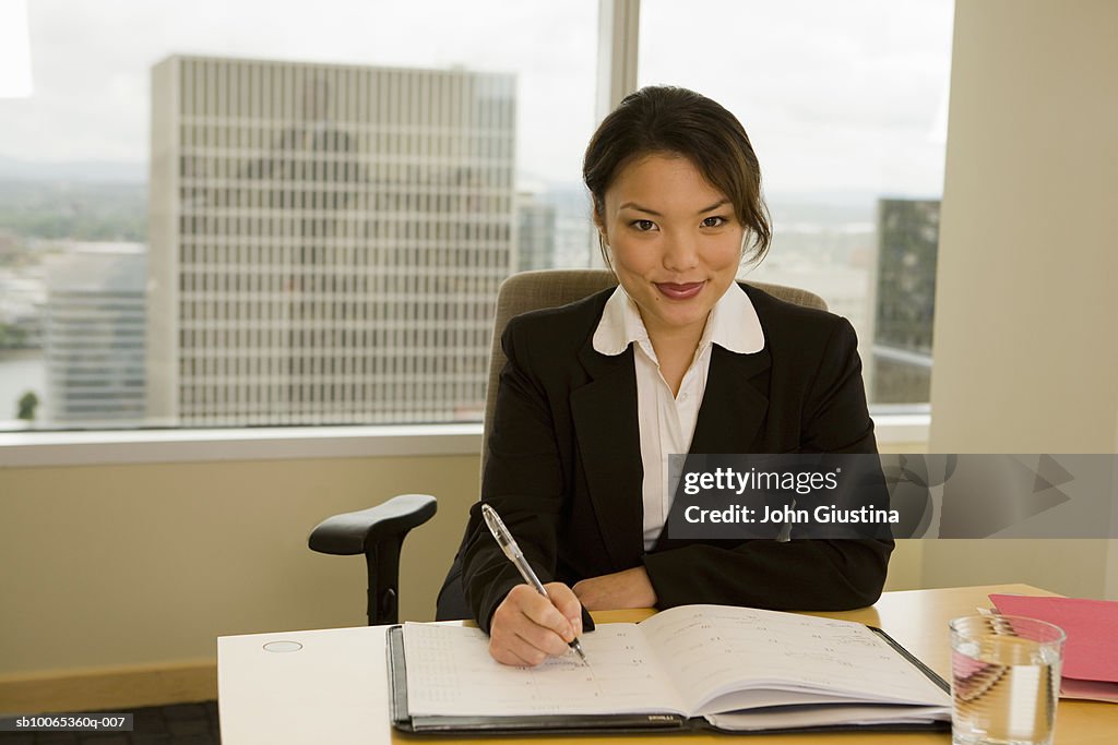Businesswoman working at desk, smiling, portrait