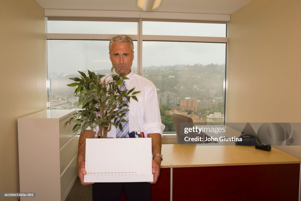 Mature man holding box and pot plant, portrait