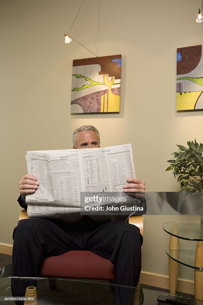 Businessman waiting in office lobby, reading newspaper